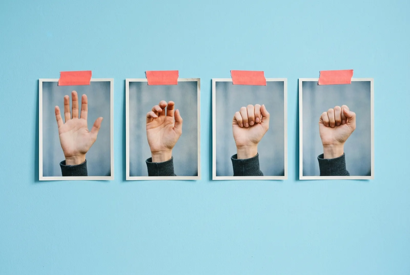 Four photographic prints of successive hand gestures attached to a light-blue wall with coral tape